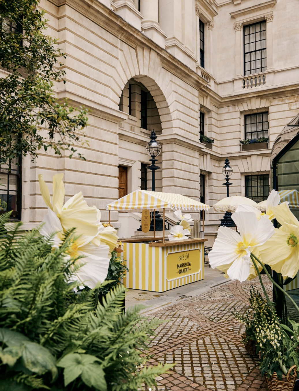 Yellow-striped Magnolia Bakery pudding cart in a grand courtyard surrounded by oversized paper flowers
